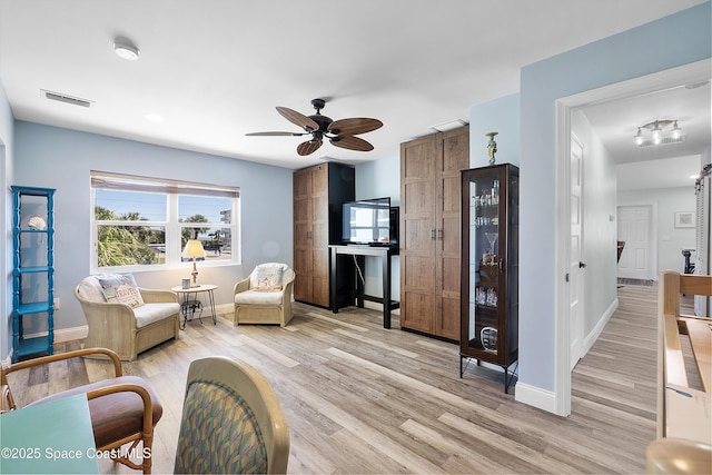 living area featuring light wood finished floors, baseboards, visible vents, and a ceiling fan