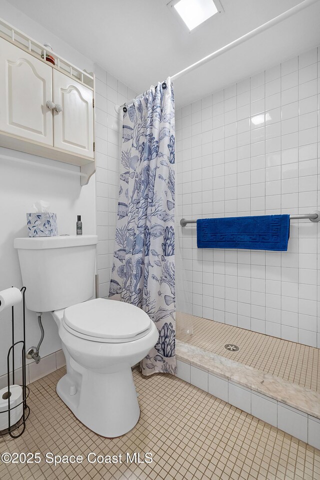 full bath with tiled shower, toilet, and tile patterned floors