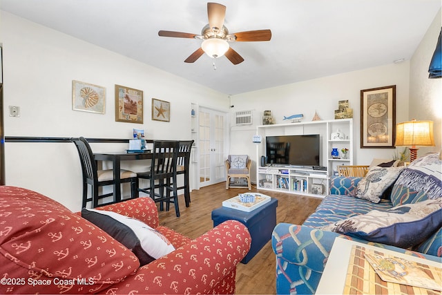 living room with a ceiling fan, a wall mounted AC, and wood finished floors