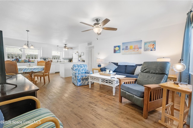 living room with ceiling fan with notable chandelier, light wood-type flooring, and visible vents