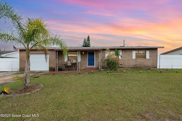 ranch-style house featuring brick siding, a lawn, an attached garage, fence, and driveway