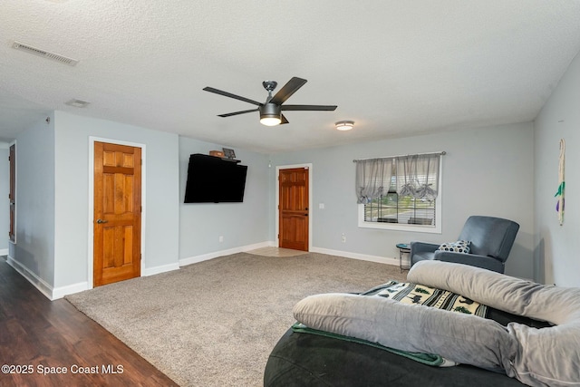 living room featuring a textured ceiling, dark wood-type flooring, a ceiling fan, visible vents, and baseboards