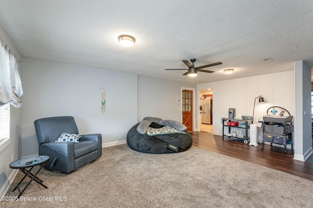 sitting room with a ceiling fan, dark colored carpet, and a textured ceiling