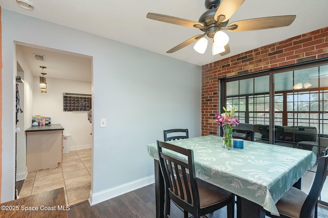 dining space with brick wall, wood finished floors, a ceiling fan, visible vents, and baseboards