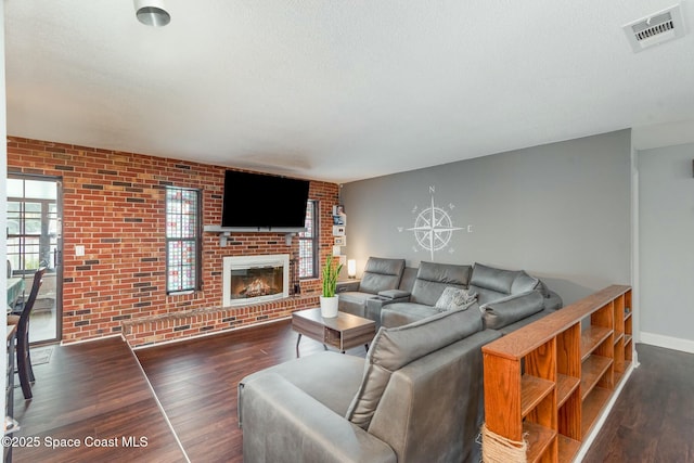 living area with baseboards, visible vents, brick wall, dark wood-type flooring, and a fireplace