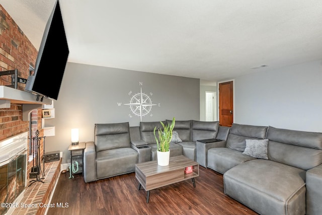 living room featuring a brick fireplace, visible vents, and wood finished floors