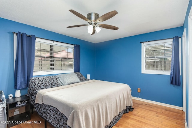 bedroom with a ceiling fan, multiple windows, baseboards, and wood finished floors