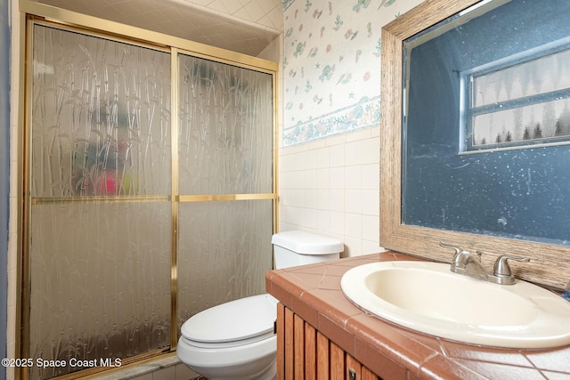 bathroom featuring tile walls, toilet, wainscoting, a shower stall, and wallpapered walls