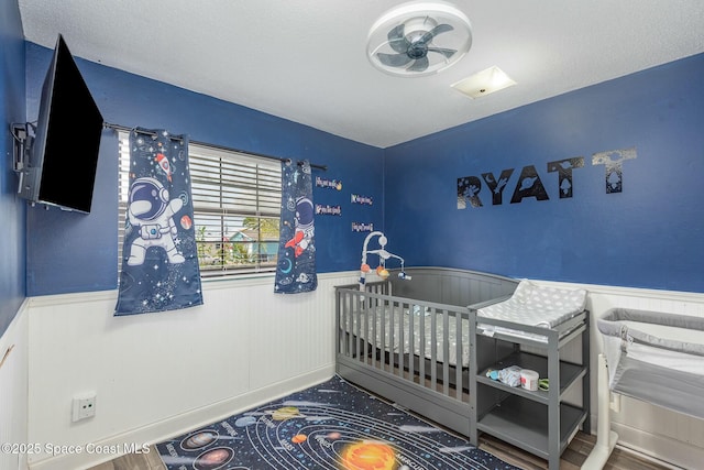 bedroom with a crib, wood finished floors, and wainscoting