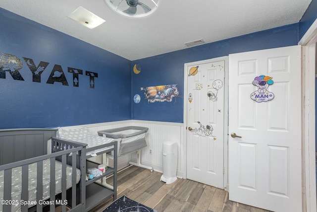 bedroom with wainscoting, visible vents, a textured ceiling, and wood finished floors