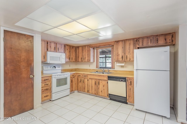 kitchen featuring white appliances, light countertops, a sink, and brown cabinetry