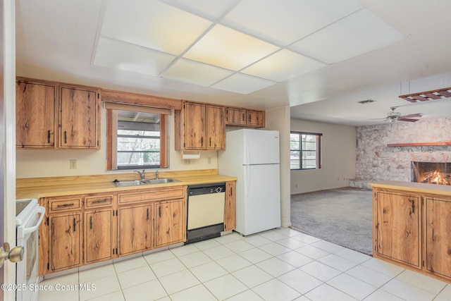 kitchen with light countertops, brown cabinetry, a sink, a stone fireplace, and white appliances