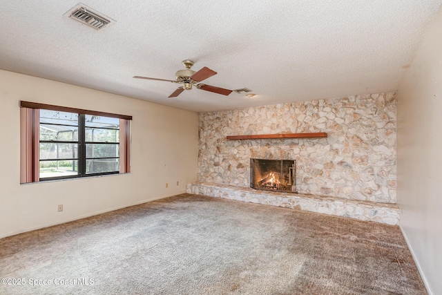 unfurnished living room with a stone fireplace, carpet, visible vents, and a ceiling fan