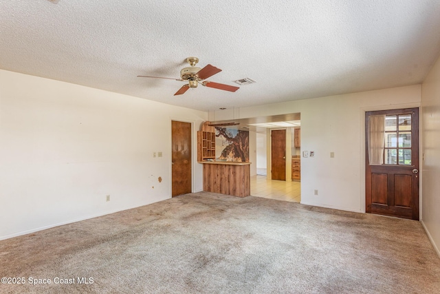 spare room featuring a ceiling fan, light colored carpet, visible vents, and a textured ceiling