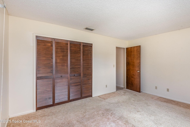 unfurnished bedroom with a closet, light colored carpet, visible vents, a textured ceiling, and baseboards