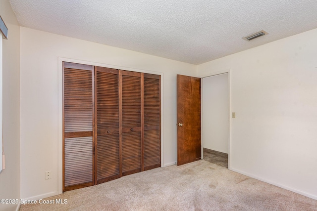 unfurnished bedroom with a closet, visible vents, carpet flooring, a textured ceiling, and baseboards