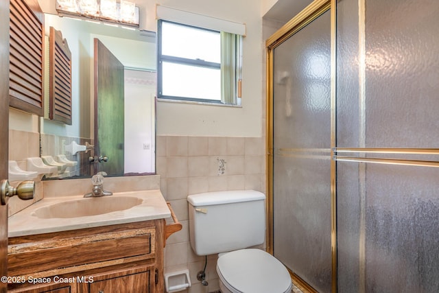 bathroom featuring toilet, vanity, tile walls, wainscoting, and an enclosed shower