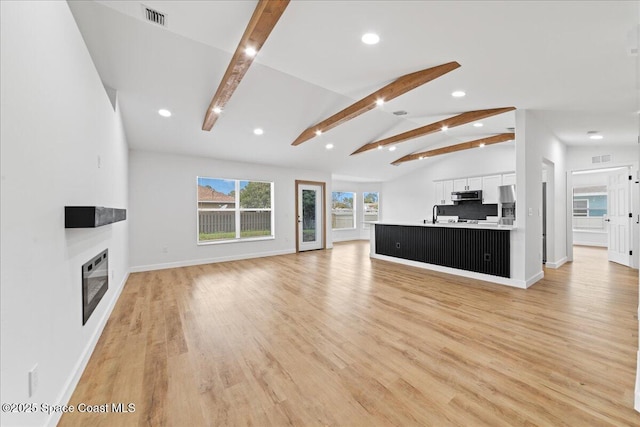 unfurnished living room with a large fireplace, visible vents, lofted ceiling with beams, heating unit, and light wood-style floors