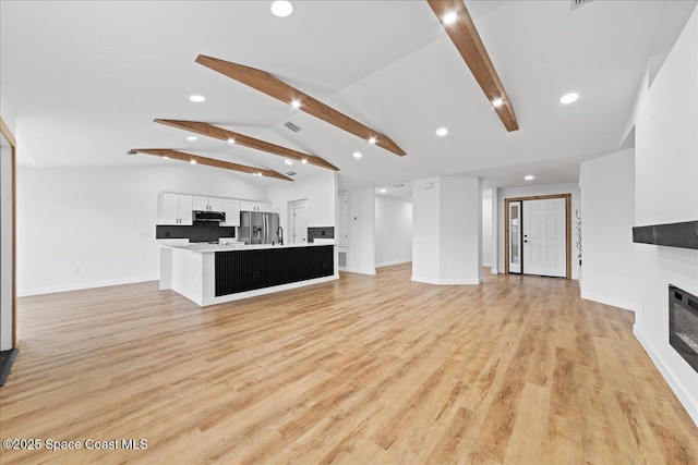 unfurnished living room with lofted ceiling with beams, light wood finished floors, baseboards, and a glass covered fireplace