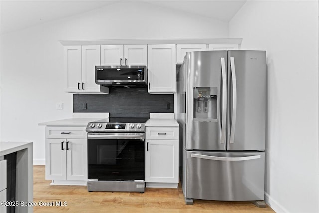 kitchen with white cabinets, vaulted ceiling, stainless steel appliances, and backsplash