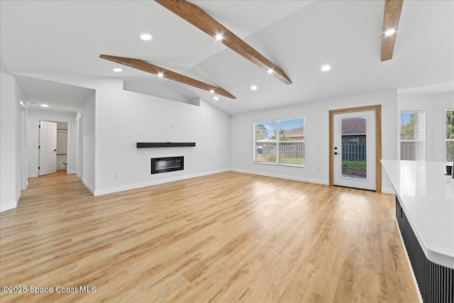 unfurnished living room with light wood-style floors, a glass covered fireplace, vaulted ceiling with beams, and baseboards