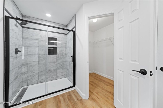 bathroom featuring a shower stall, a spacious closet, baseboards, and wood finished floors