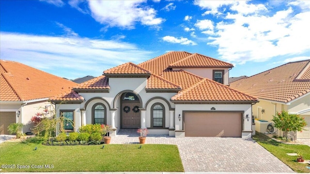 mediterranean / spanish-style home with a tiled roof, an attached garage, decorative driveway, a front lawn, and stucco siding