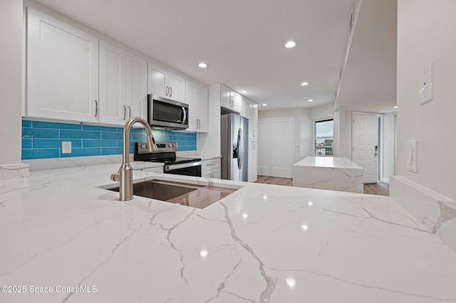 kitchen featuring stainless steel appliances, recessed lighting, tasteful backsplash, a sink, and light stone countertops