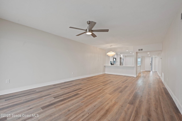 unfurnished living room with light wood-style flooring, visible vents, baseboards, and ceiling fan with notable chandelier