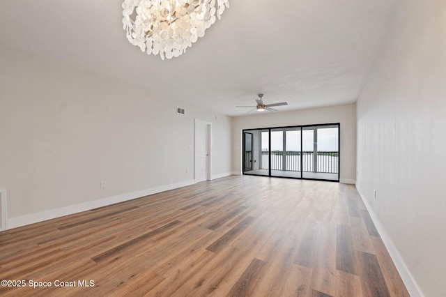 spare room featuring light wood-type flooring, visible vents, baseboards, and ceiling fan with notable chandelier