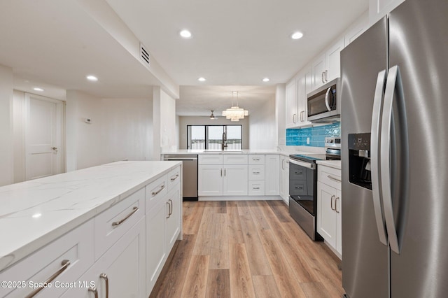 kitchen with light stone counters, stainless steel appliances, tasteful backsplash, light wood-style flooring, and white cabinets