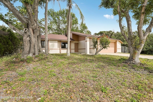 mid-century home featuring a garage, a front lawn, driveway, and stucco siding