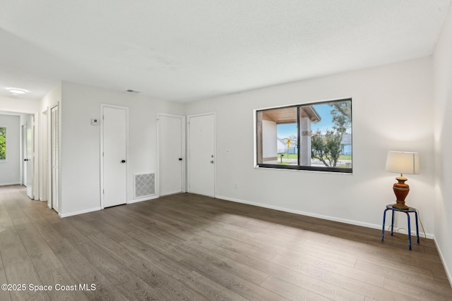 empty room featuring plenty of natural light, wood finished floors, visible vents, and baseboards