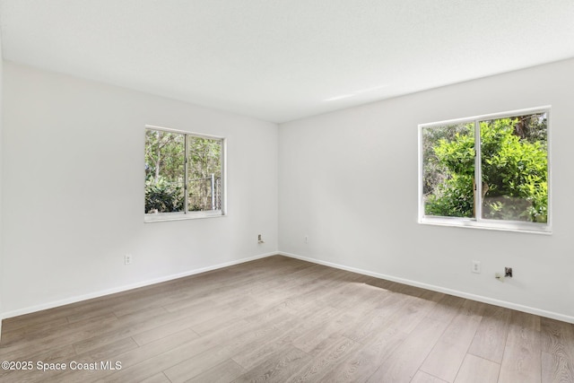 spare room featuring plenty of natural light, baseboards, and wood finished floors