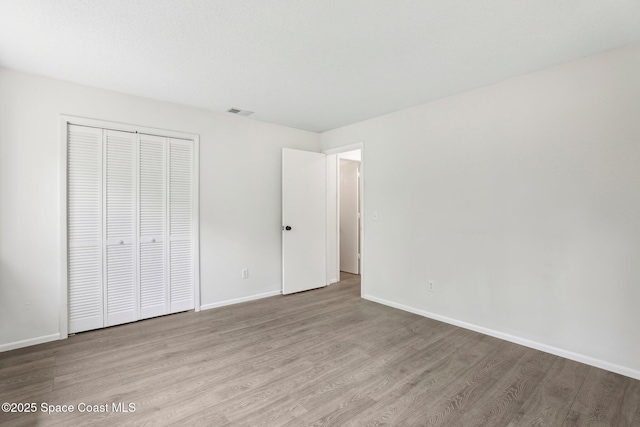 unfurnished bedroom with a closet, visible vents, baseboards, and wood finished floors