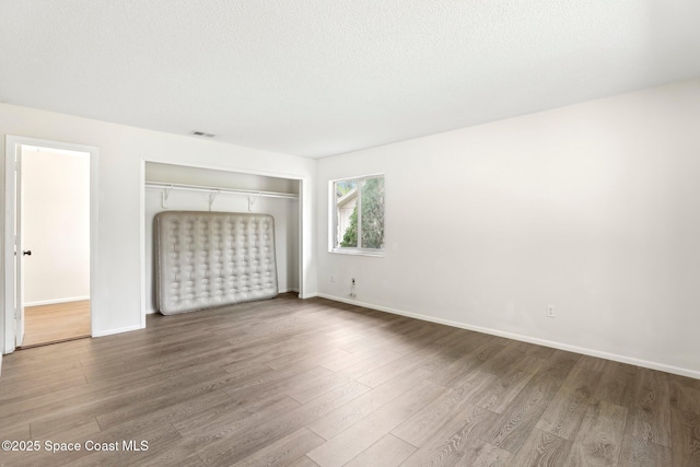 unfurnished bedroom featuring baseboards, wood finished floors, a closet, and a textured ceiling