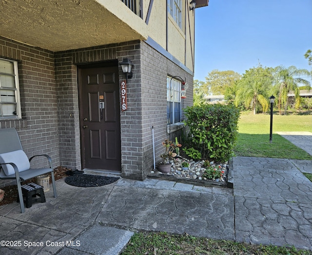 entrance to property featuring brick siding, a lawn, and a patio