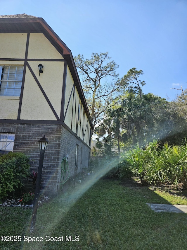 view of property exterior featuring brick siding, a lawn, and stucco siding