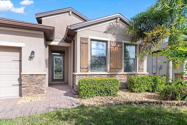 view of exterior entry with a garage, stone siding, and stucco siding