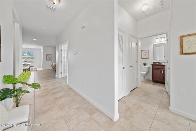 hall featuring visible vents, baseboards, and light tile patterned floors