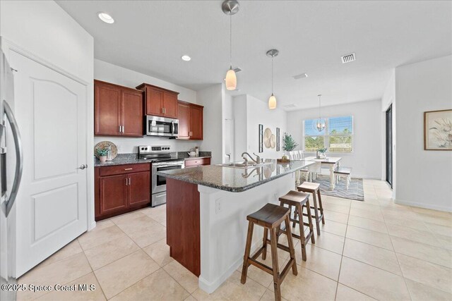 kitchen with stainless steel appliances, a sink, visible vents, a kitchen breakfast bar, and dark countertops