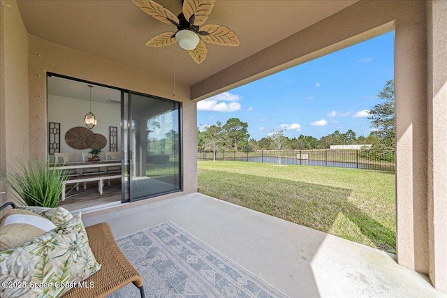 view of patio with a water view, fence, and ceiling fan