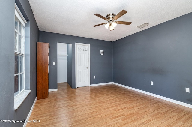 unfurnished room with light wood finished floors, baseboards, visible vents, and a textured ceiling