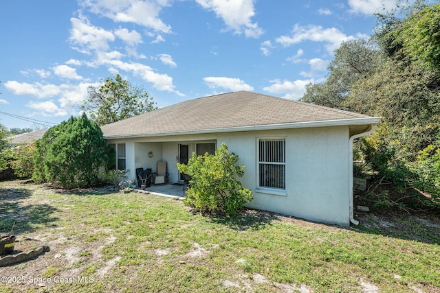 back of house with roof with shingles, a lawn, and stucco siding