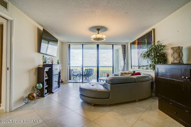 living room with light tile patterned floors, a wall of windows, a textured ceiling, and a glass covered fireplace