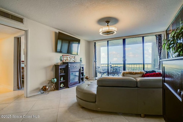 living area featuring a textured ceiling, light tile patterned flooring, visible vents, expansive windows, and a glass covered fireplace