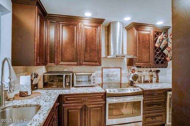 kitchen featuring stainless steel electric stove, a sink, backsplash, light stone countertops, and wall chimney exhaust hood