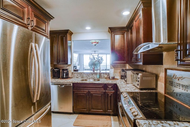 kitchen featuring stainless steel appliances, tasteful backsplash, a sink, wall chimney range hood, and light stone countertops