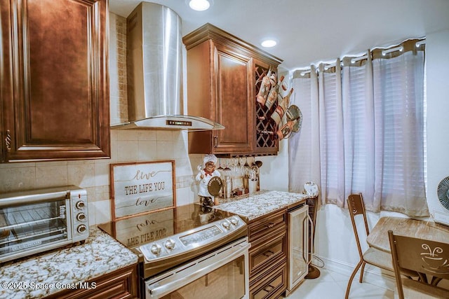 kitchen featuring a toaster, backsplash, light stone countertops, stainless steel electric range oven, and wall chimney exhaust hood