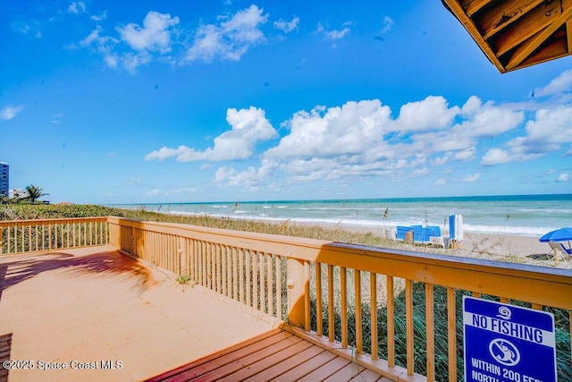 wooden terrace featuring a water view and a beach view